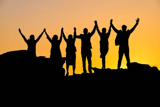 Silhouetten van een groep mensen die hand in hand naast elkaar staan bij zonsondergang